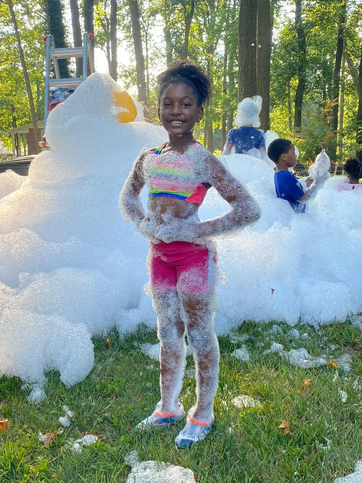 Girl striking a confident pose while covered in foam on a backyard lawn after playing at a foam party