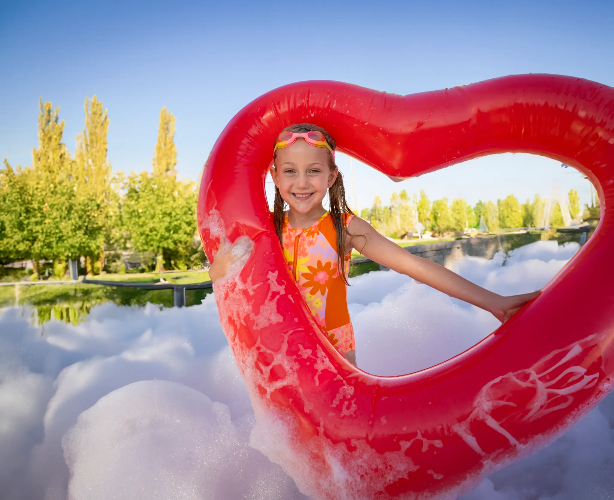 Smiling girl framed by a red heart-shaped inflatable while playing in foam outdoors