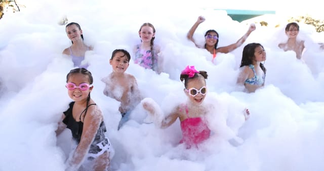 a group of kids smiling and cheering chest-deep in foam at an NJ backyard party