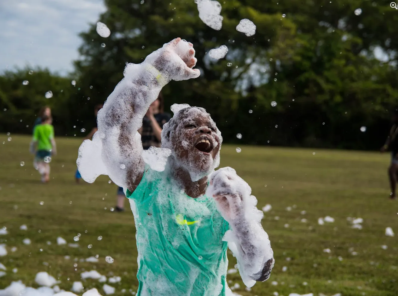 Boy running through a field of foam with arms outstretched and big smile at a foam party on a sunny day