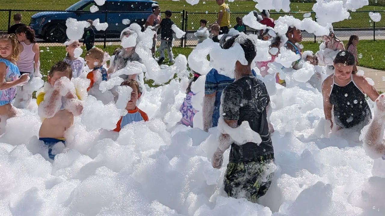 a large group of kids playing together in a wide field of foam at an outdoor birthday party in NJ