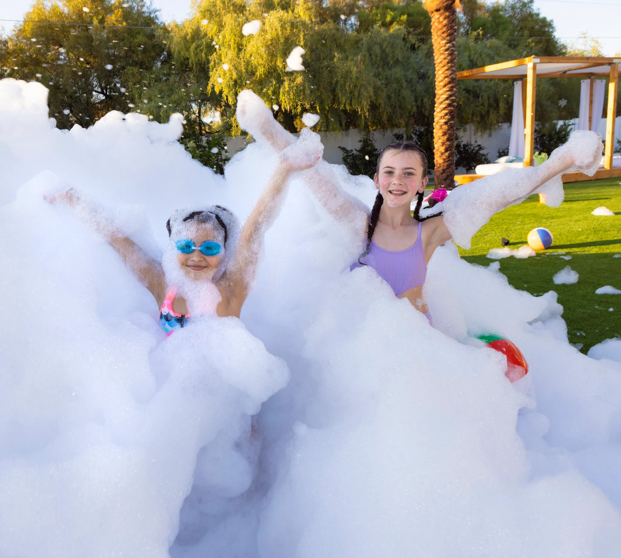 Two girls with arms raised bursting out of foam at a backyard foam party in Haddonfield, NJ