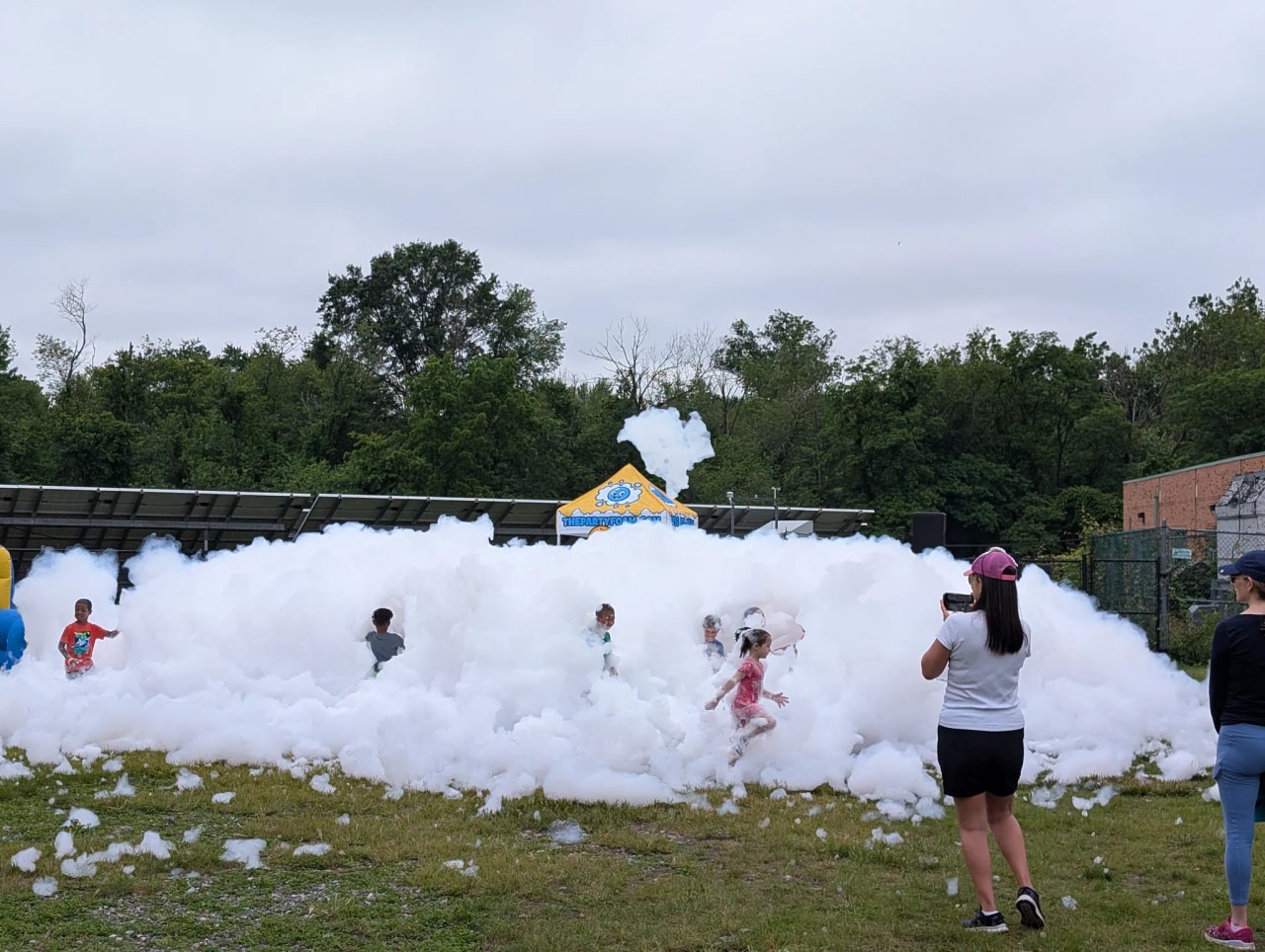Group of kids playing in a large foam cloud at a school field day while a parent takes photos nearby
