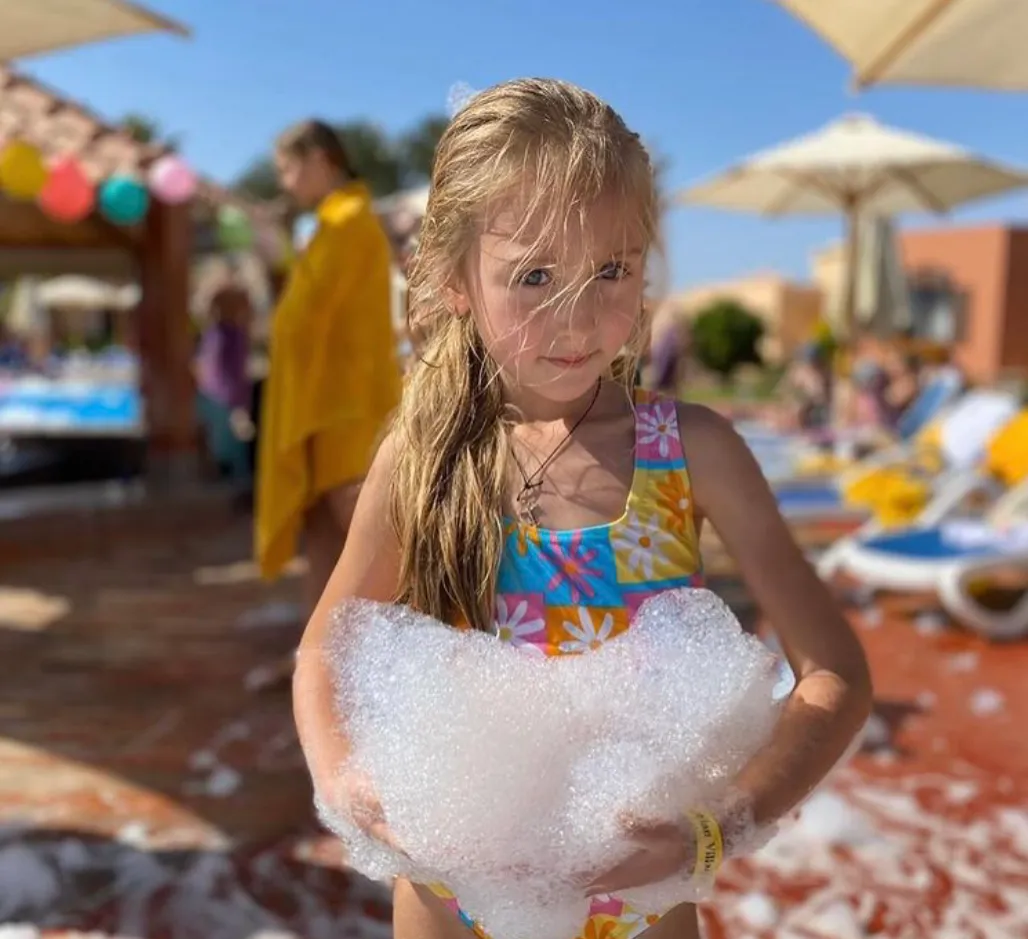 Young girl in a swimsuit holding a clump of foam at an outdoor foam pit party