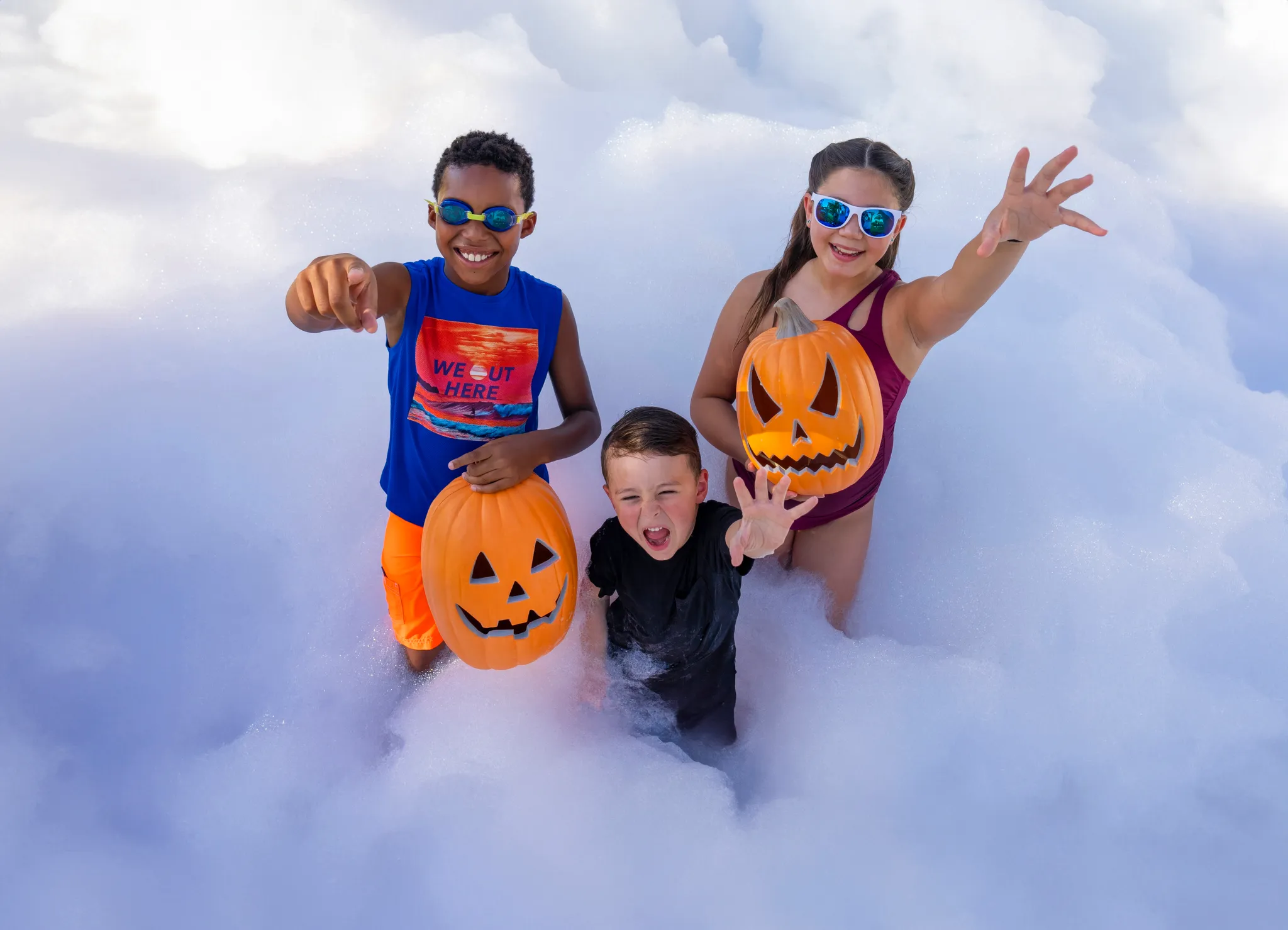Three kids with pumpkin buckets smiling and posing in deep foam at an outdoor foam birthday party